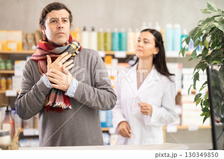 man with a scarf tied around his throat stands in a pharmacy against the background of pharmacist man with a scarf tied around his throat stands in a pharmacy against the background of pharmacist 130349850