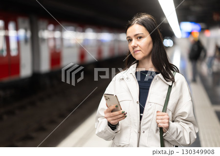 Woman stands with smartphone at subway station Woman stands with smartphone at subway station 130349908