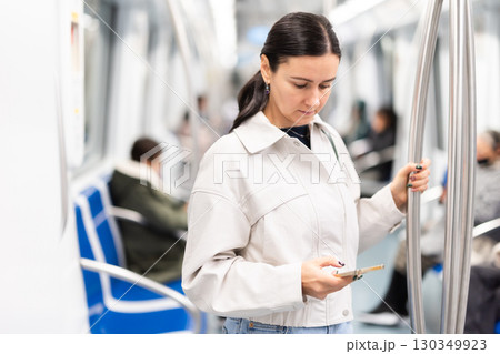 Woman stand in metro carriage, scrolls through social media feed Woman stand in metro carriage, scrolls through social media feed 130349923
