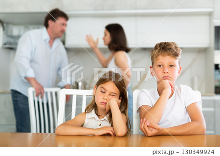 Two children sitting at the kitchen table sadly while their parents quarrelling Two children sitting at the kitchen table sadly while their parents quarrelling 130349924