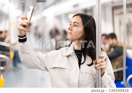 In the subway car, woman with mobile phone makes a selfie or scans QR code In the subway car, woman with mobile phone makes a selfie or scans QR code 130349928