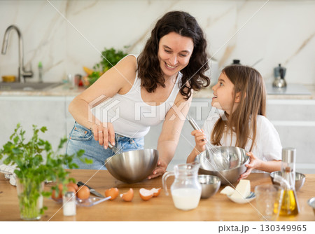 Happy mother and her daughter whisking ingredients in metal bowl in the kitchen 130349965