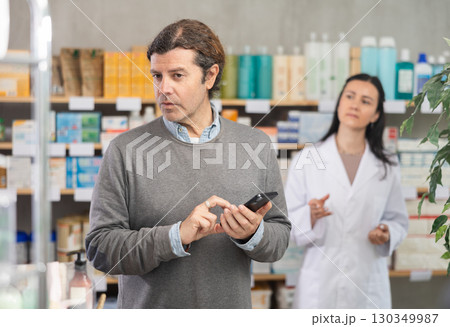 Male customer looking for something in drugstore. Female pharmacist offers him medicines Male customer looking for something in drugstore. Female pharmacist offers him medicines 130349987