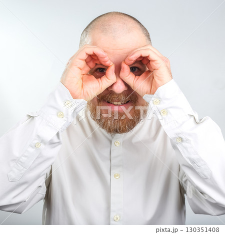 Man making binoculars with hands, smiling, and engaging in playful gesture indoors 130351408
