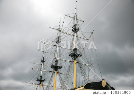 Tall ship masts pierce cloudy sky above historic vessel in port during overcast afternoon 130351900