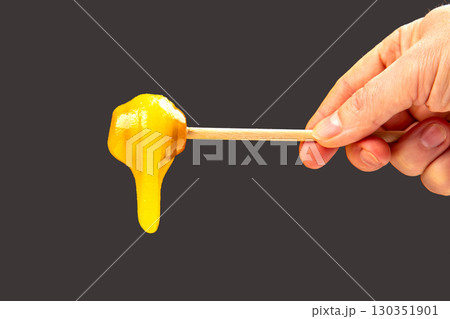 Hand holding a stick with golden melted candy syrup dripping down 130351901