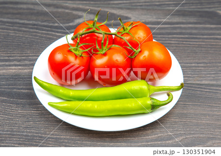 Fresh tomatoes and green peppers on a white plate arranged on a wooden table 130351904