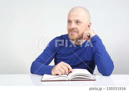 Man with beard reading a book and thinking in a bright room during daytime Man with beard reading a book and thinking in a bright room during daytime 130351916