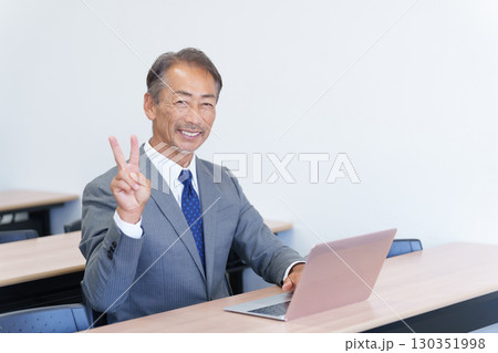 パソコンを使いピースサインをするシニアビジネスマン 130351998