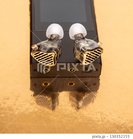 High-end audio equipment with transparent earbuds resting on a golden surface 130352155