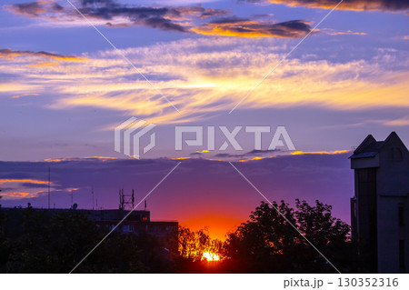 Colorful sunset over urban skyline with clouds and trees visible in the background 130352316