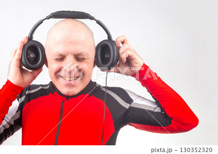 Man enjoying music while wearing headphones and a cycling outfit indoors Man enjoying music while wearing headphones and a cycling outfit indoors 130352320