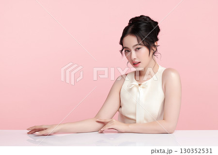 A beautiful young Asian woman with clean, fresh skin against a pink background. Skincare, facial treatment, cosmetology, beauty, and spa. An elegant portrait of an Asian woman. 130352531