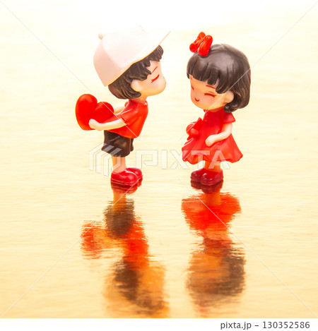 Miniature figures of a boy and girl sharing a romantic moment on a reflective surface Miniature figures of a boy and girl sharing a romantic moment on a reflective surface 130352586