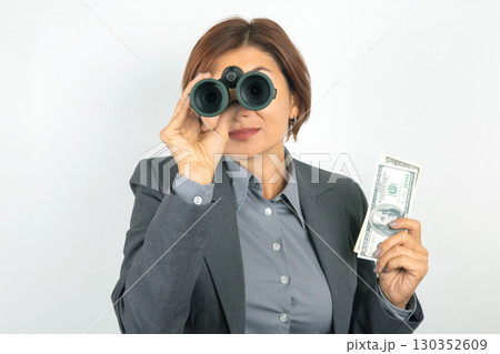 Businesswoman in professional attire with cash and binoculars, spotting opportunities 130352609