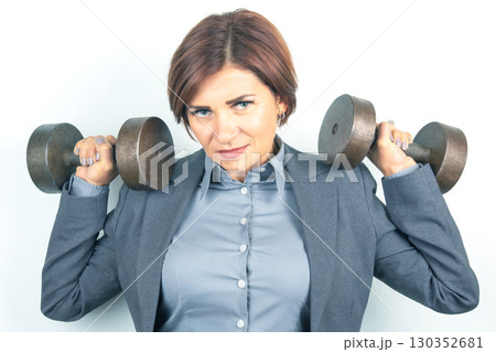 Strong businesswoman lifting weights indoors in a professional outfit Strong businesswoman lifting weights indoors in a professional outfit 130352681