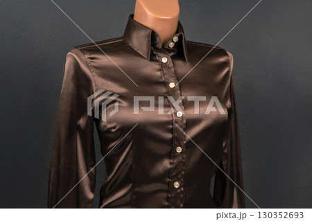 Elegant dark brown satin shirt displayed on a mannequin against a dark backdrop 130352693