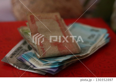 Stacked and folded Indian rupee notes on a red background, used as a sacred offering during worship, puja ceremonies, and cultural traditions. Stacked and folded Indian rupee notes on a red background, used as a sacred offering during worship, puja ceremonies, and cultural traditions. 130352897