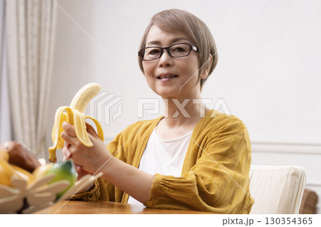 ダイニングでバナナを剥いて食べるシニア女性  130354365