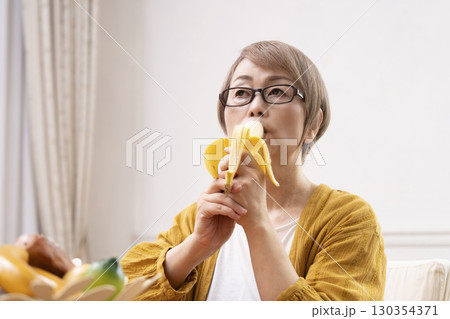ダイニングでバナナを剥いて食べるシニア女性  130354371