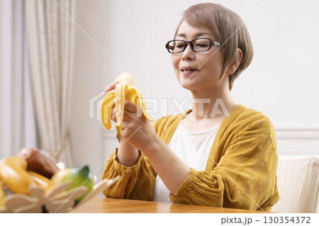 ダイニングでバナナを剥いて食べるシニア女性 ダイニングでバナナを剥いて食べるシニア女性 130354372