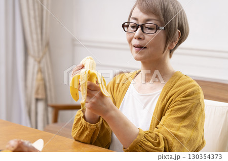 ダイニングでバナナを剥いて食べるシニア女性 ダイニングでバナナを剥いて食べるシニア女性 130354373
