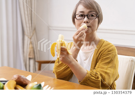 ダイニングでバナナを剥いて食べるシニア女性  130354379