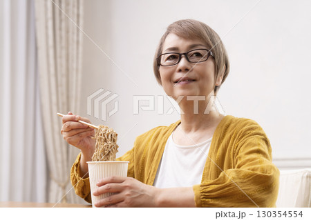 ダイニングでインスタント麺を食べるシニア女性 ダイニングでインスタント麺を食べるシニア女性 130354554