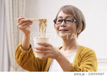 ダイニングでインスタント麺を食べるシニア女性 130354567