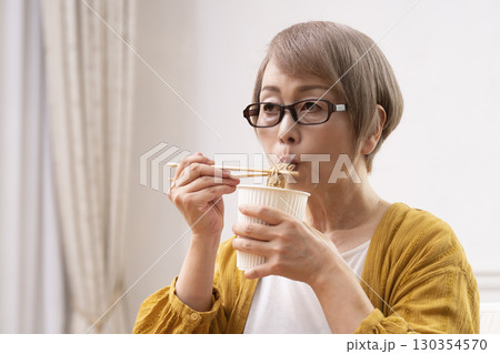 ダイニングでインスタント麺を食べるシニア女性 130354570