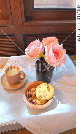 Coffee cup, cookie bowl, pink rose vase resting on white tablecloth beside window, radiating warm, intimate morning moment Coffee cup, cookie bowl, pink rose vase resting on white tablecloth beside window, radiating warm, intimate morning moment 130354632
