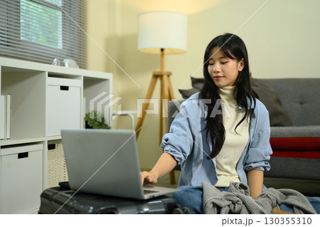 Young woman sitting on the floor with a suitcase, using a laptop to plan and organize her trip Young woman sitting on the floor with a suitcase, using a laptop to plan and organize her trip 130355310