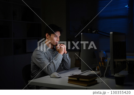 Serious office worker staying late at workplace, concentrating on computer screen Serious office worker staying late at workplace, concentrating on computer screen 130355420