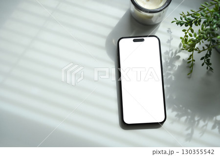Smartphone with blank screen placed on white desk, decorated with plant and candle 130355542