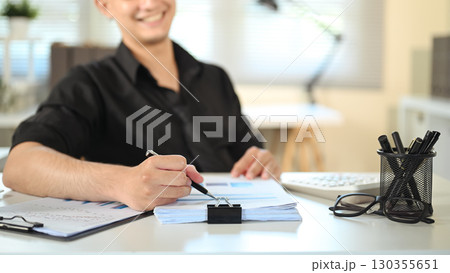 Male employee reviewing business report with glasses and stationery on desk 130355651