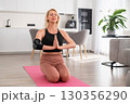 Blonde middle aged woman in sportswear performing namaste pose on pink yoga mat at home, focusing on balance, breathing, and mindfulness 130356290