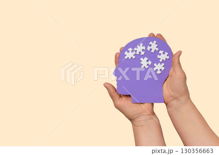 Hands hold a purple head silhouette featuring white puzzle pieces Hands hold a purple head silhouette featuring white puzzle pieces 130356663