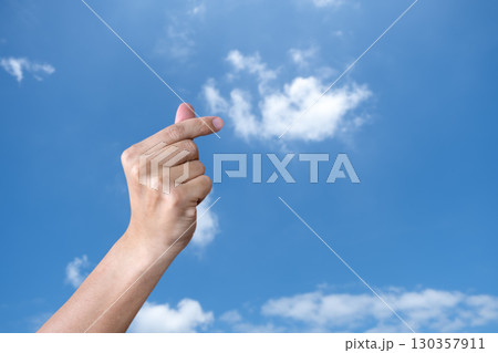 Hand Making Korean Finger Heart Gesture Against Blue Sky 130357911