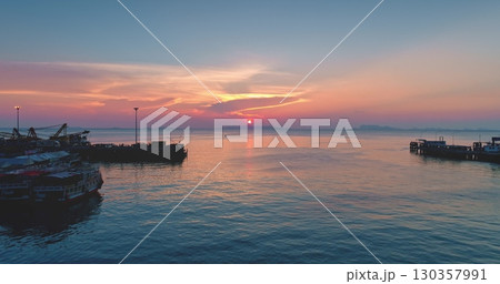 Tranquil seascape at sunset with colorful sky reflecting on the calm water of the Gulf of Thailand, with silhouettes of piers, boats, and cranes creating a peaceful and scenic view Tranquil seascape at sunset with colorful sky reflecting on the calm water of the Gulf of Thailand, with silhouettes of piers, boats, and cranes creating a peaceful and scenic view 130357991