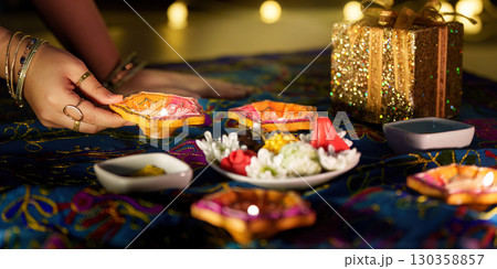 Diwali rituals. Hand placing decorative diyas on a festive table with sweets. 130358857
