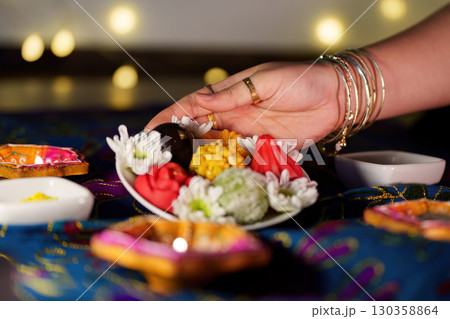 Diwali festivities. Hands placing sweets on a decorative plate for celebration. 130358864