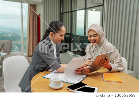 Two businesswomen are collaborating in a modern office to share ideas and ambitions Two businesswomen are collaborating in a modern office to share ideas and ambitions 130358959