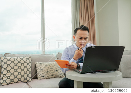 A Business Professional Engaged in Remote Work Utilizing a Laptop and Taking Notes A Business Professional Engaged in Remote Work Utilizing a Laptop and Taking Notes 130359063