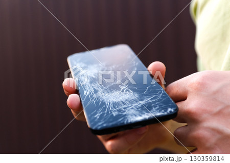 a male hand holding a phone with a broken screen. broken phone screen repair. male hand holding shattered smartphone. mobile device damage problem 130359814