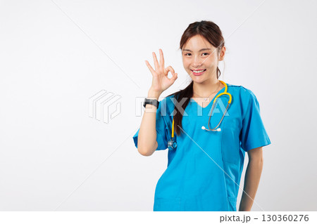 Young asian nurse, ok sign, friendly woman smile is showing her approval with an OK gesture while wearing blue scrubs, a stethoscope and a happy young nurse, headshot isolated studio white background 130360276