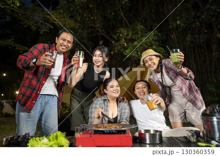 Indonesian southeast asian people relaxing together outdoors and enjoying refreshing drinks while cooking sliced beef on a grill pan. The scene of the lifestyle of enjoying food in a natural setting Indonesian southeast asian people relaxing together outdoors and enjoying refreshing drinks while cooking sliced beef on a grill pan. The scene of the lifestyle of enjoying food in a natural setting 130360359