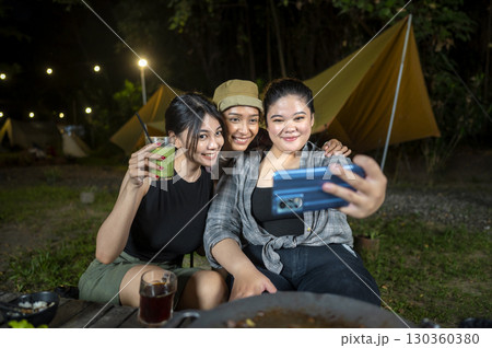 Indonesian southeast asian women capturing a selfie using a cellphone together outdoors and enjoying refreshing drinks. The scene of the lifestyle of enjoying food in a natural setting 130360380