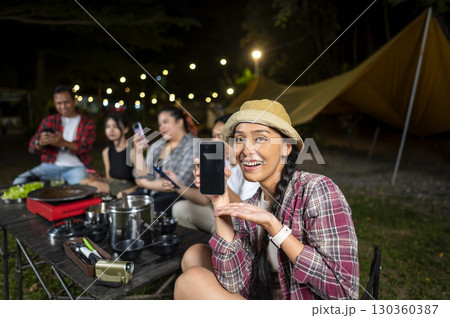 Indonesian southeast asian people enjoying a camping at night, using their cellphones to capture moments and share experiences. One of them showed her cellphone display. Mockup or Copy space Indonesian southeast asian people enjoying a camping at night, using their cellphones to capture moments and share experiences. One of them showed her cellphone display. Mockup or Copy space 130360387