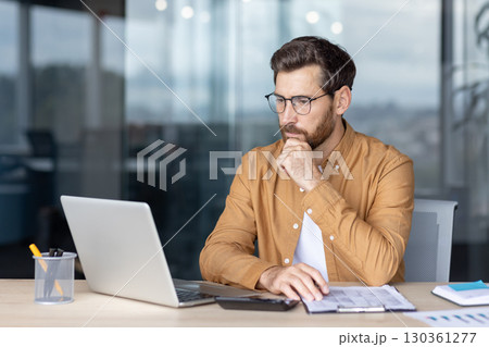 Focused professional sits at a desk in a contemporary office space, working on a laptop while contemplating tasks. The atmosphere conveys concentration, productivity, and dedication to work. Focused professional sits at a desk in a contemporary office space, working on a laptop while contemplating tasks. The atmosphere conveys concentration, productivity, and dedication to work. 130361277