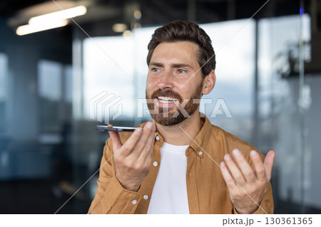 A professional man interacts with a smartphone, using its voice command feature, in an office environment with contemporary decor and natural lighting. A professional man interacts with a smartphone, using its voice command feature, in an office environment with contemporary decor and natural lighting. 130361365